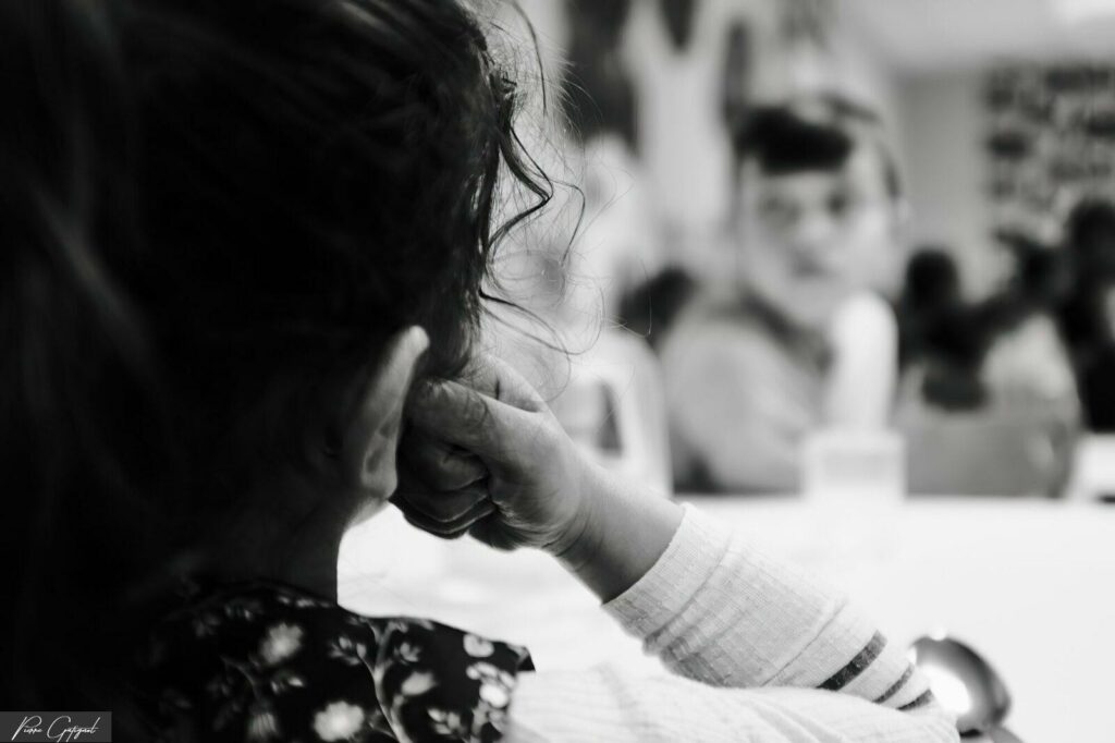 Enfant vu de dos, main au visage, personnes floues au fond